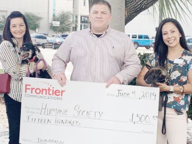 A man holds a large check from Frontier and stands in between two women who are holding two puppies.