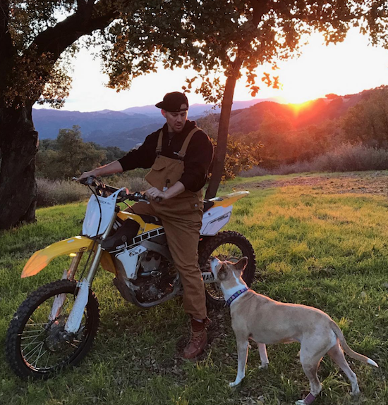 Channing Tatum sits on a dirt bike and smiles down at his pit bull with the sunset in the background